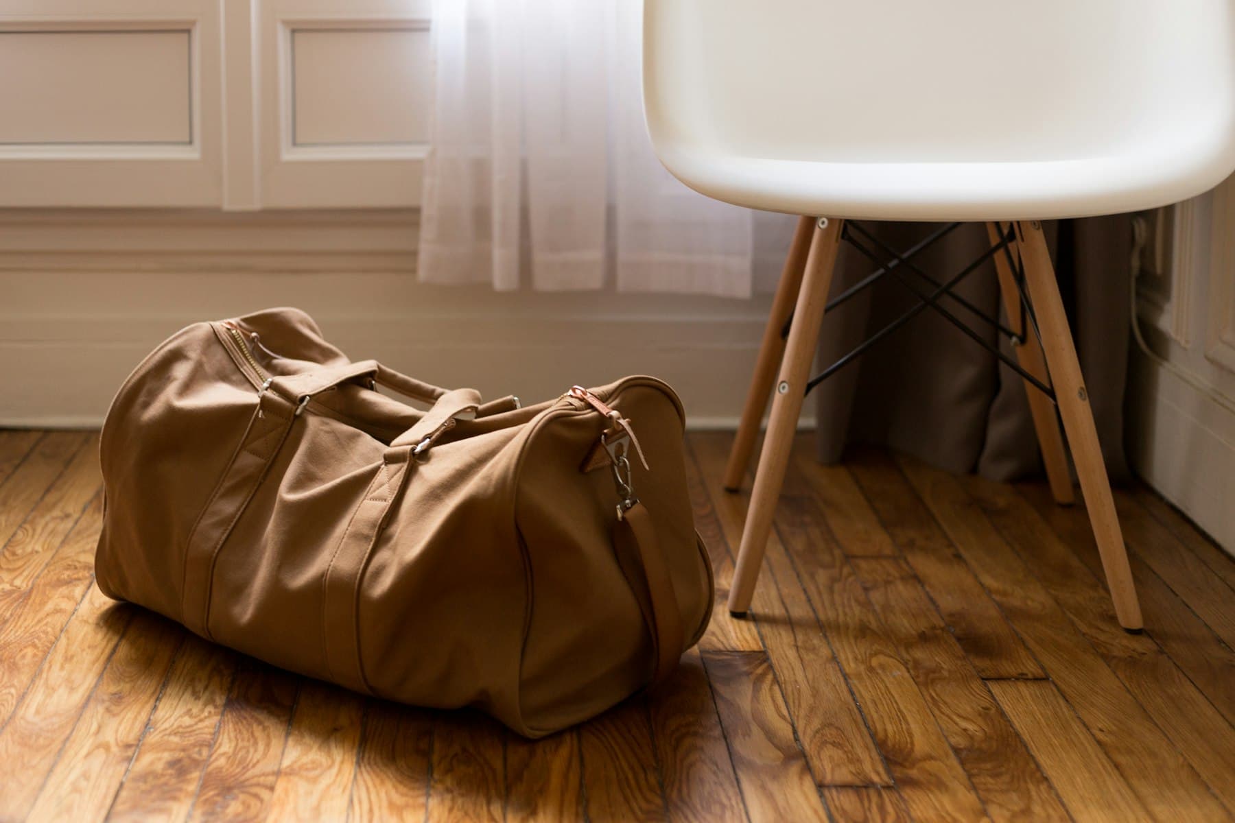 Brown leather duffel bag ready for travel beside a chair