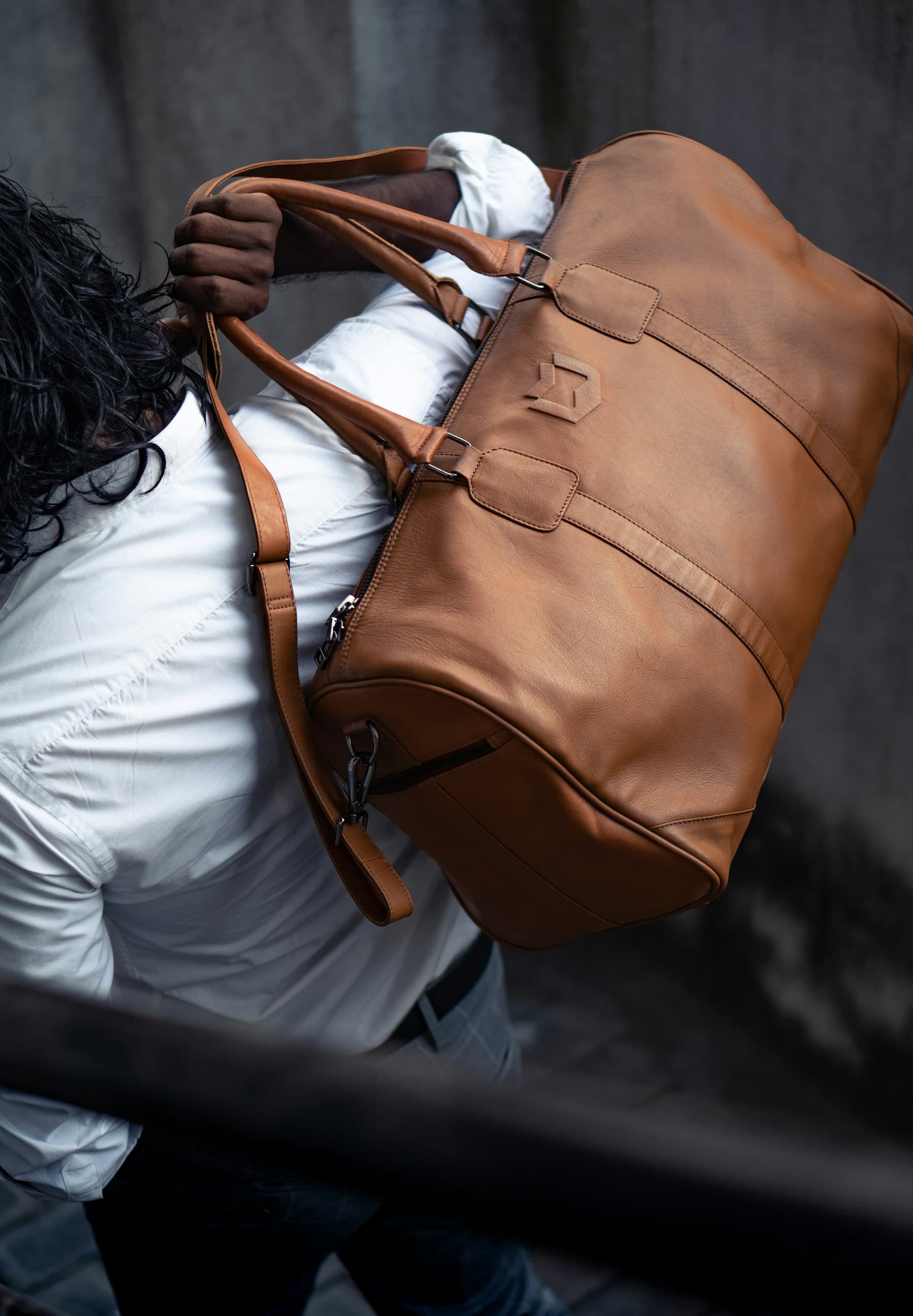 Traveler carrying a large brown leather duffel bag